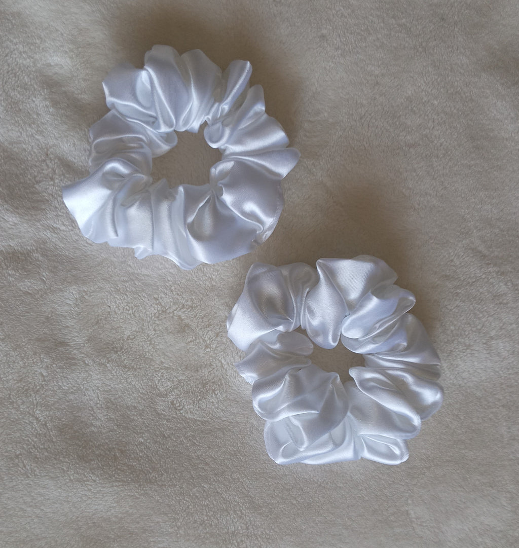Two white satin scrunchies on a beige fabric background