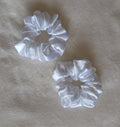 Two white satin scrunchies on a beige fabric background